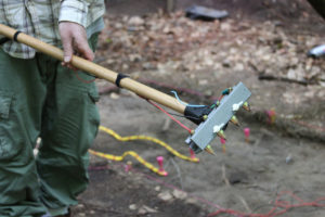 An American University graduate student holds a piece of experimental geophysical equipment that was designed specifically for use at the Nameless site. The idea was to noninvasively examine intact soils in excavation units after the thick layer of tree roots were removed. These roots often obscured data that was produced from typical geophysical survey done from the ground surface. The data from this technique is still being analyzed but early indications were that it was a moderate success. Credit: GDSLS/Dan Sayers 2013