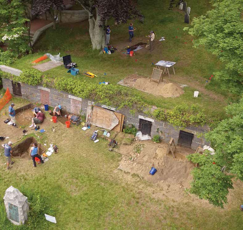 An aerial view of the excavations on Burial Hill. The grey structure with the black and brick doors is an 1830s burial vault that cuts through the site. Excavations in front of and behind the vault revealed a series of building postholes, trash pits, and many seventeenthcentury artifacts from the original settlement. Native American and English pottery was found in the trash pits, suggesting the use of Native pots in the English houses. Credit: Bruce T. Martin.