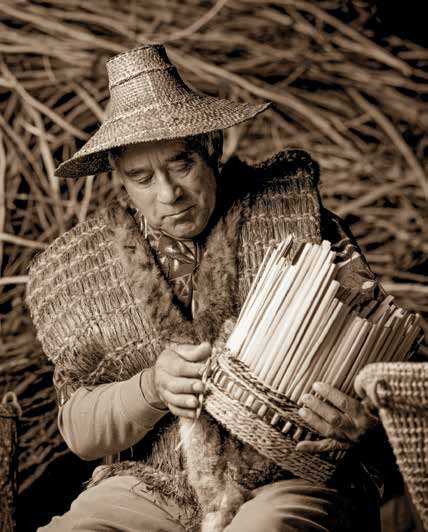Ed Carriere weaves a cattail basket. He also wove the cedar-bark vest and cedar-bark hat he’s wearing. Credit: FREDRICK DENT