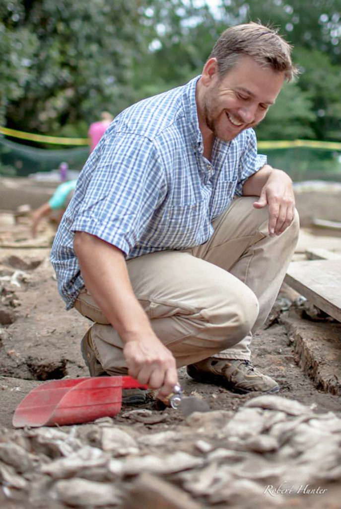 Colonial Williamsburg Foundation Senior Staff Archaeologist Mark Kostro excavates a pit feature filled with oyster shells adjacent to the Wren Building at the College of William and Mary. The discarded shells were left by early eighteenth-century William & Mary students. Credit: Rob Hunter.