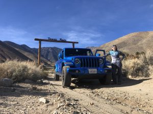 Photo of a woman standing next to a blue Jeep that is parked in front of the entrance to the Arbegast-Tunawee Ranch.
