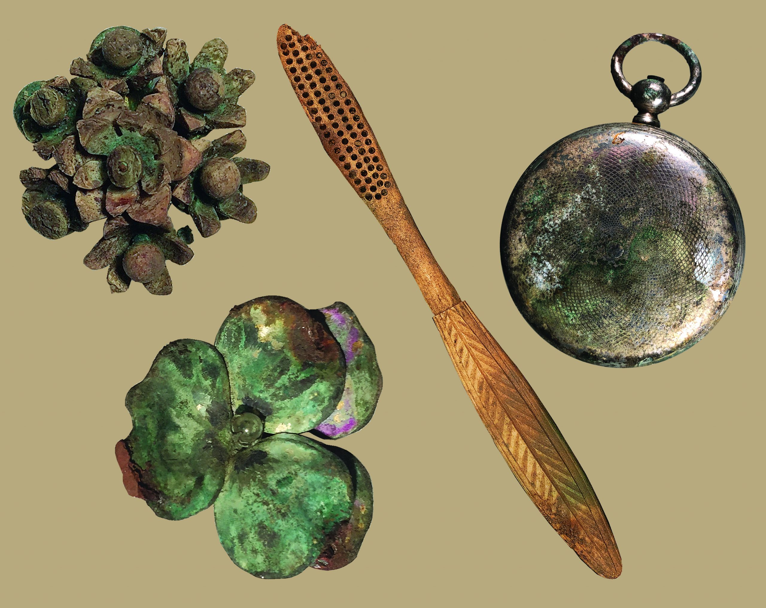photo showing two carved floral brooches that are tarnished, a wooden toothbrush, and a silver pocketwatch