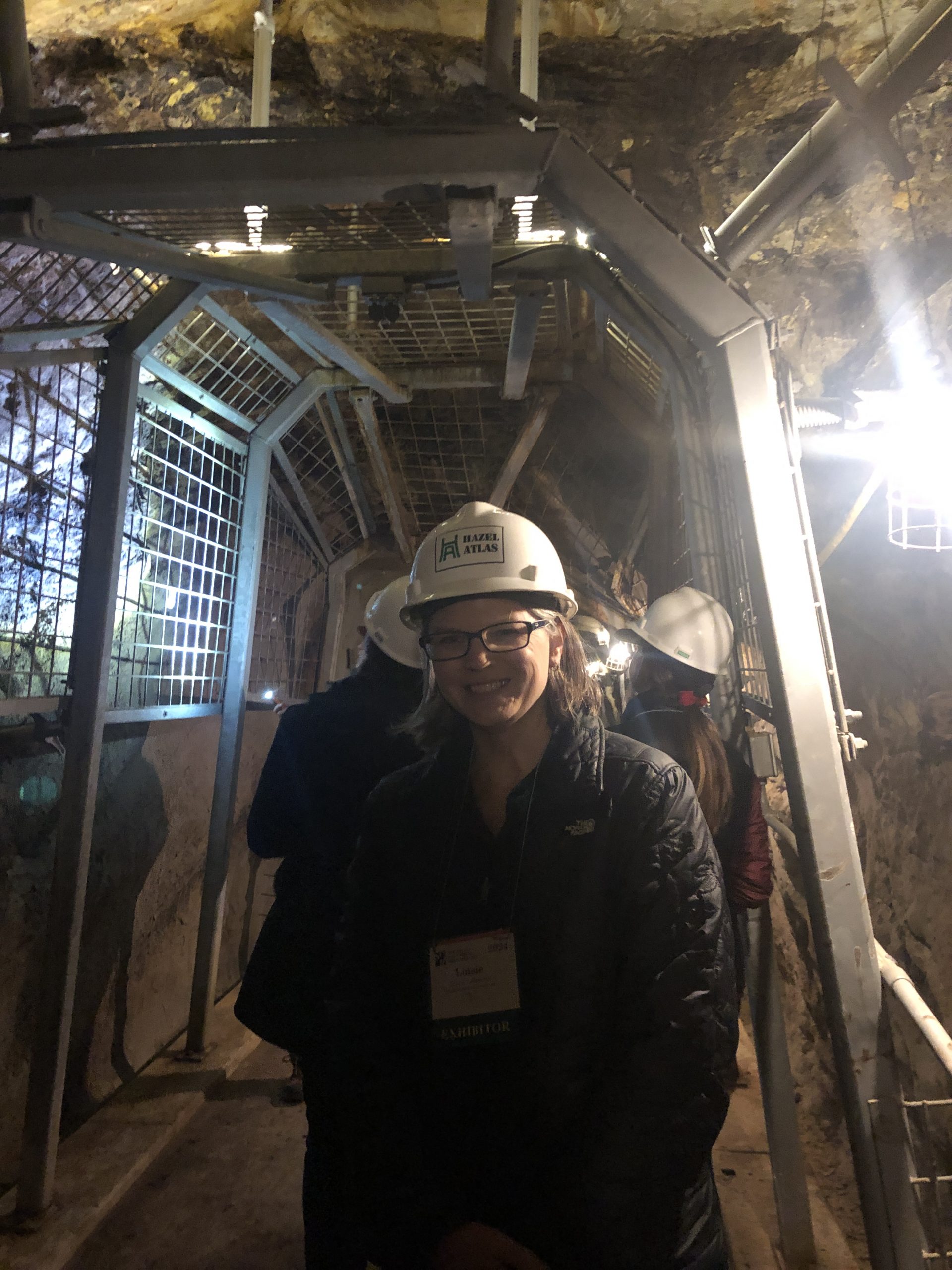 photo of woman wearing a white hardhat and standing inside a tunnel lit by a bright light on the right-hand side of the photo